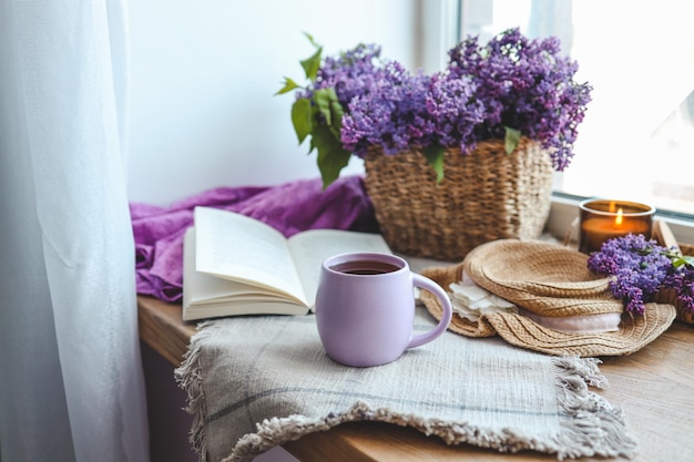 Taza de té sombrero de paja libro abierto y canasta de lila primavera naturaleza muerta