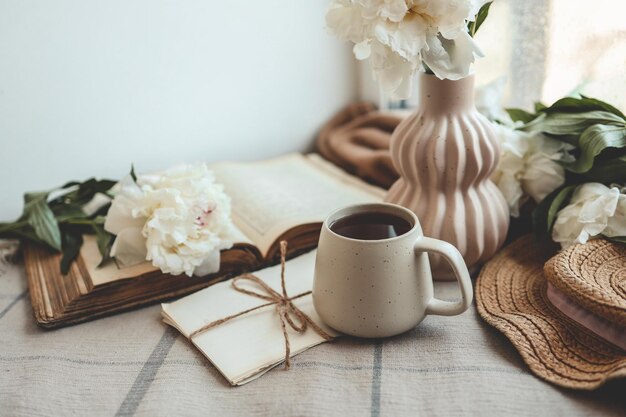 Taza de té sombrero de paja libro abierto y peonías bodegón de primavera