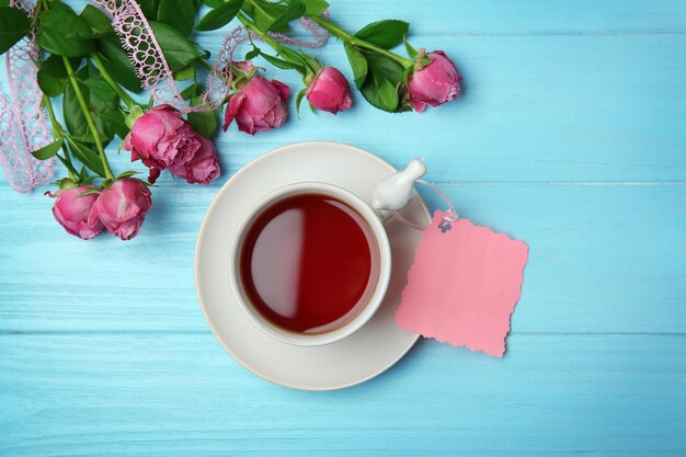 Taza de té tarjeta vacía y rosas en la vista superior de fondo de madera