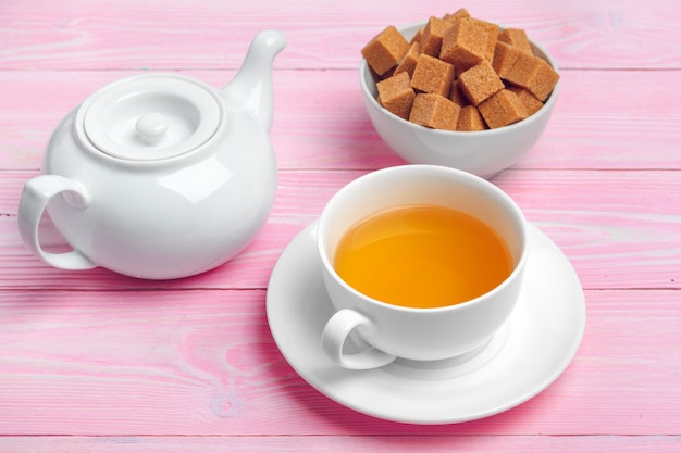 Taza de té con terrones de azúcar y ramas de flores en la mesa de madera de cerca