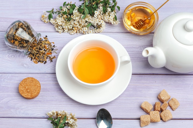 Taza de té con terrones de azúcar y ramas de flores en la mesa de madera de cerca