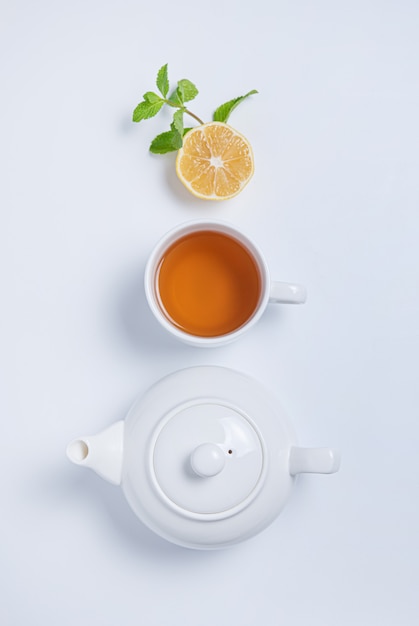 Taza de té y tetera con limón y menta sobre fondo blanco. Vista superior y espacio de copia
