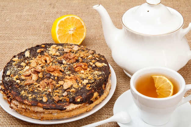 Taza de té, tetera de porcelana y pastel de hojaldre de chocolate casero en mesa con cilicio