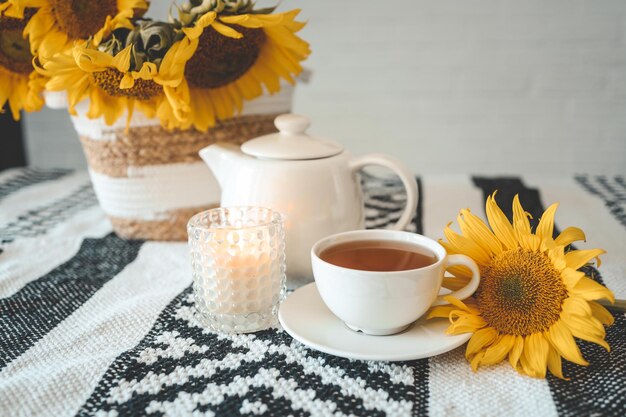 Una taza de té y una tetera con una vela sobre una mesa con estética de girasoles a la hora del té.