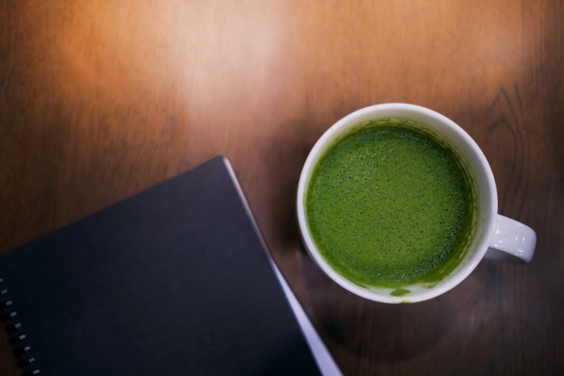 Taza de té verde caliente con leche y cuaderno sobre la mesa en la casa o cafetería