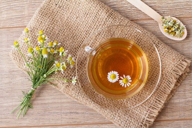 Taza de té verde con flores de manzanilla blanca y bolsa sobre fondo de madera. Vista superior