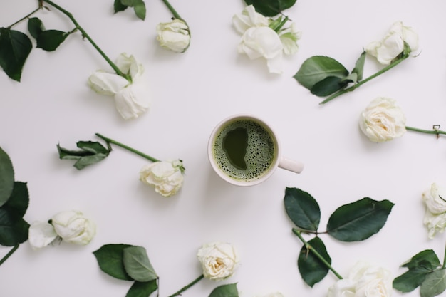 Una taza de té verde con rosas blancas sobre fondo blanco. Flatlay, vista superior, espacio de copia.