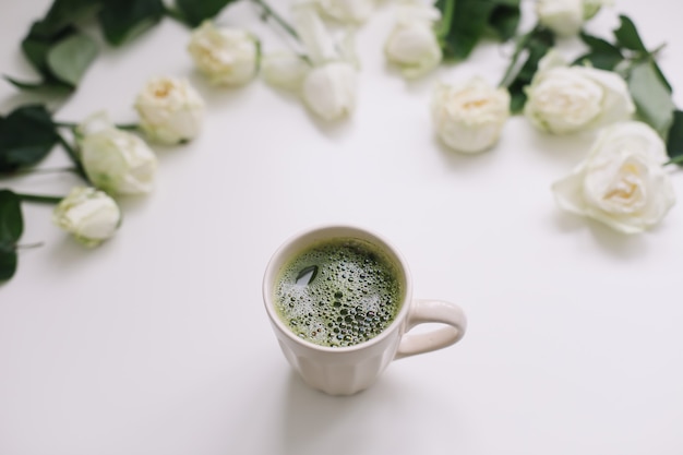 Una taza de té verde con rosas blancas sobre superficie blanca