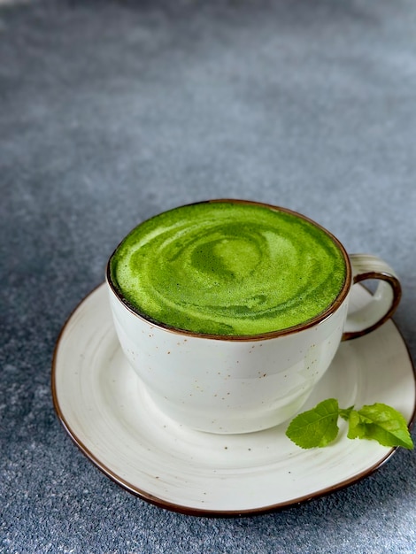 Una taza de té verde sobre un platillo con una hoja sobre ella, un café con leche matcha verde sobre un fondo oscuro