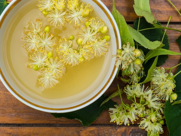 Taza de té verde y tilo sobre fondo de madera, útil concepto de medicina popular de flores de tilo