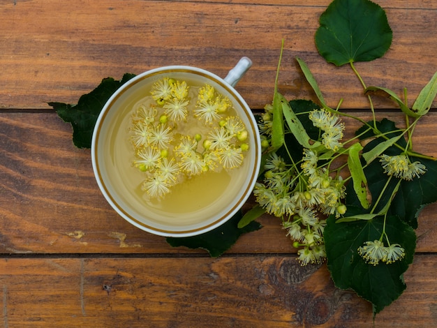 Taza de té verde y tilo sobre fondo de madera, útil concepto de medicina popular de flores de tilo
