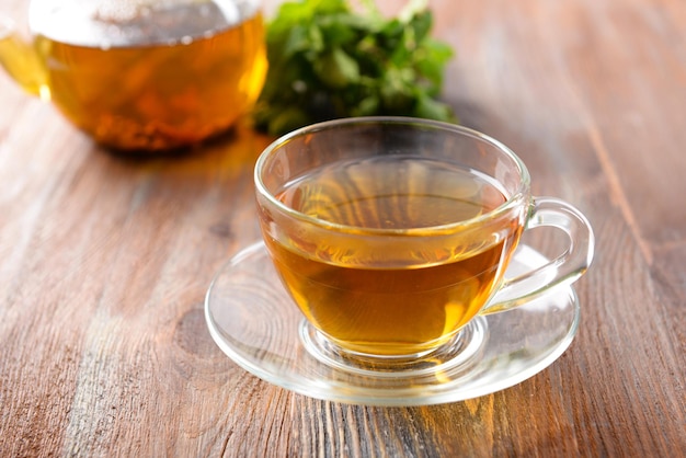 Taza de té de vidrio con hojas verdes sobre fondo de madera