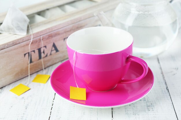 Taza y tetera con bolsitas de té en primer plano de la mesa de madera