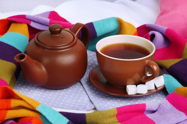 Taza y tetera con pañuelo en la cama de cerca