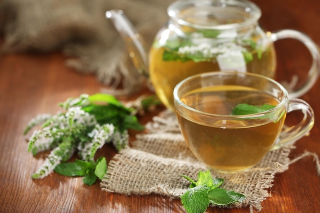 Taza y tetera de té de hierbas con flores de menta fresca en la mesa de madera