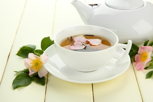 Taza y tetera de té de hierbas con flores de rosa de la cadera en la mesa de madera blanca