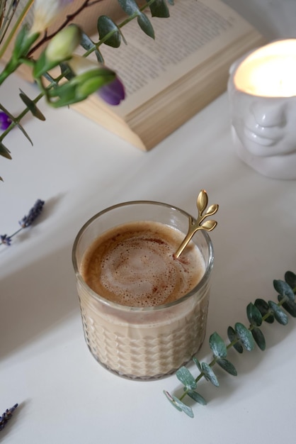 Taza de textura de vidrio con café con leche cerca de jarrón con ramo en la mesa en la cocina