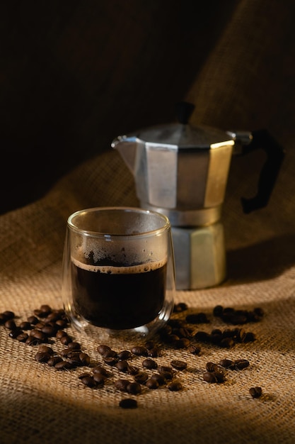 Una taza transparente con café y una cafetera de géiser sobre un fondo oscuro