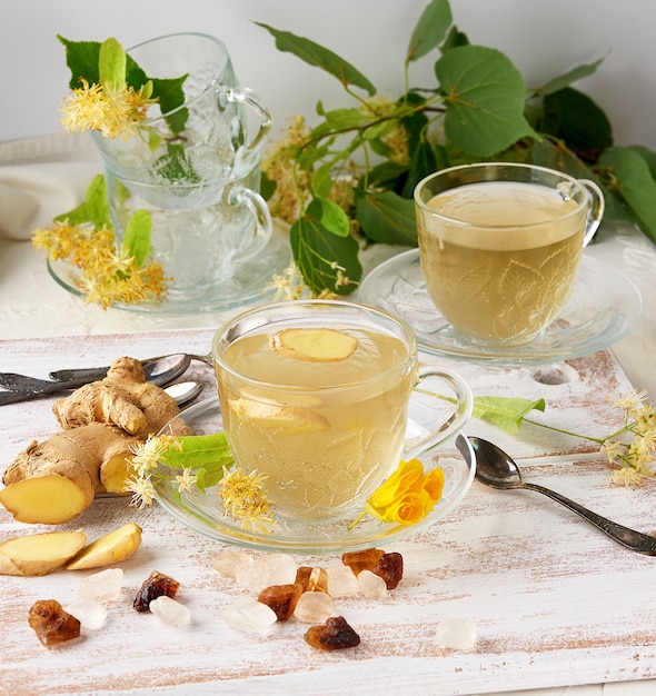 Taza transparente de té de tilo a base de hierbas y trozos de jengibre en una tabla de madera blanca