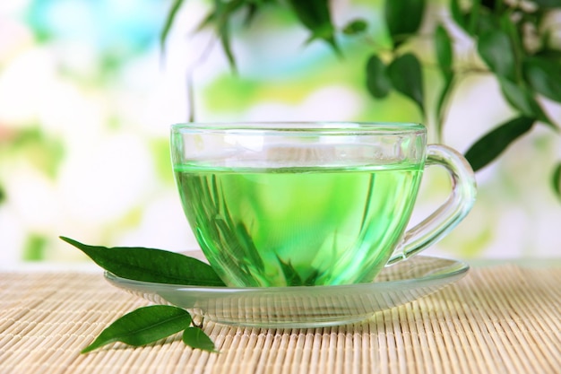 Taza transparente de té verde en la estera de bambú en el fondo de la naturaleza