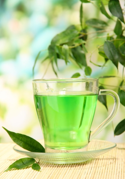 Taza transparente de té verde en la estera de bambú en el fondo de la naturaleza