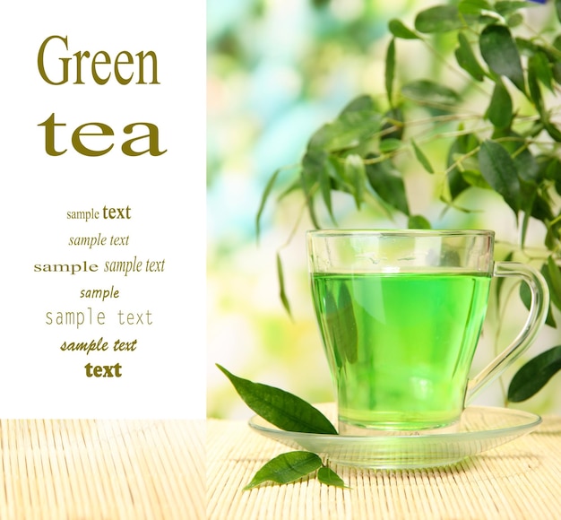 Taza transparente de té verde en la estera de bambú en el fondo de la naturaleza