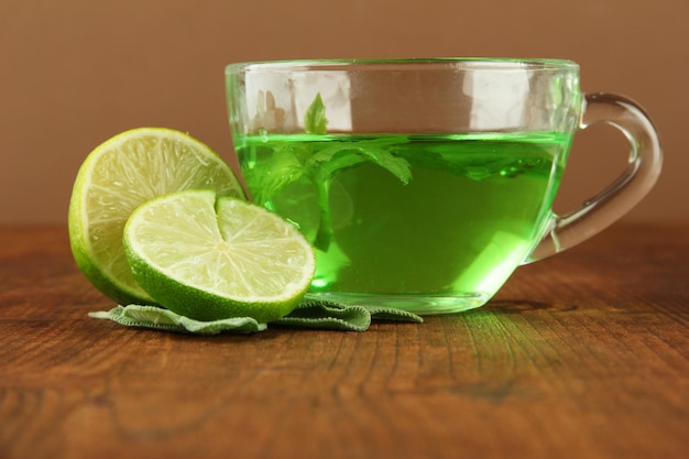 Taza transparente de té verde con lima y salvia en la mesa sobre fondo marrón