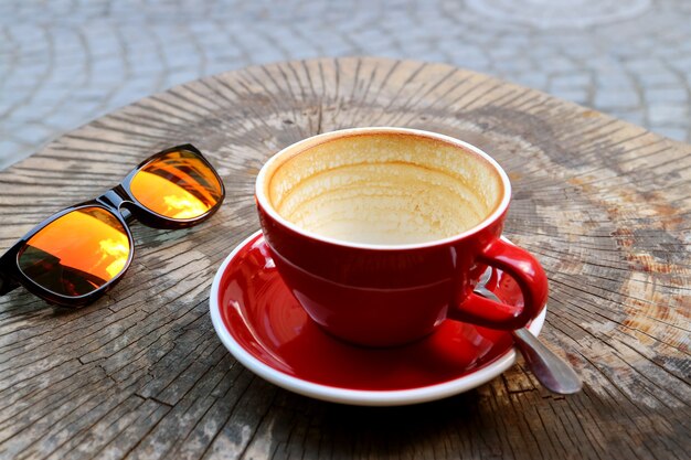 Taza vacía de café terminado de beber aislado en la mesa del tocón de árbol con gafas de sol