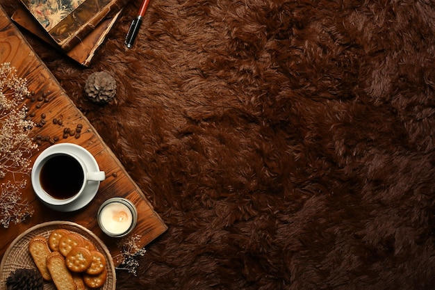 Taza de velas aromáticas de galletas de café y libros sobre alfombra mullida