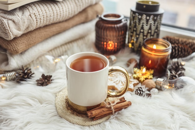 Una taza de velas encendidas de té caliente y una pila de suéteres de punto en la foto estética del alféizar de la ventana