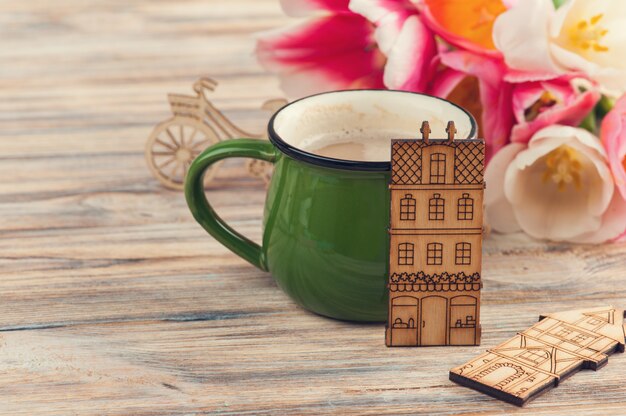 Taza verde de café, tulipanes y casas de madera de juguete.