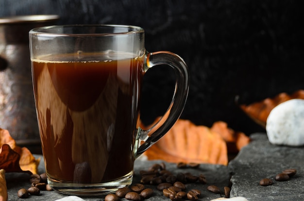 Una taza de vidrio de café fuertemente elaborado sobre las piedras con granos de café y hojas de otoño. Enfoque selectivo.