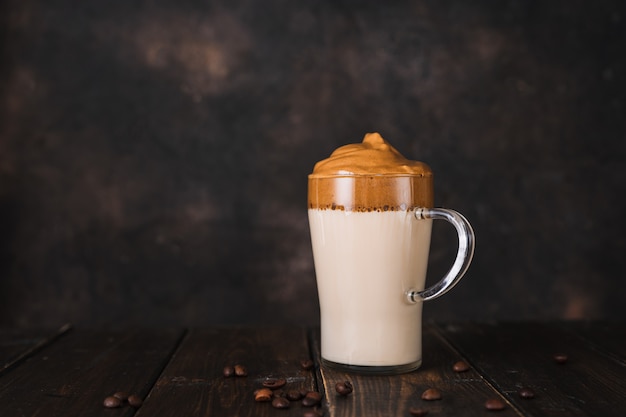 Una taza de vidrio de café instantáneo batido Dalgona sobre fondo rústico oscuro