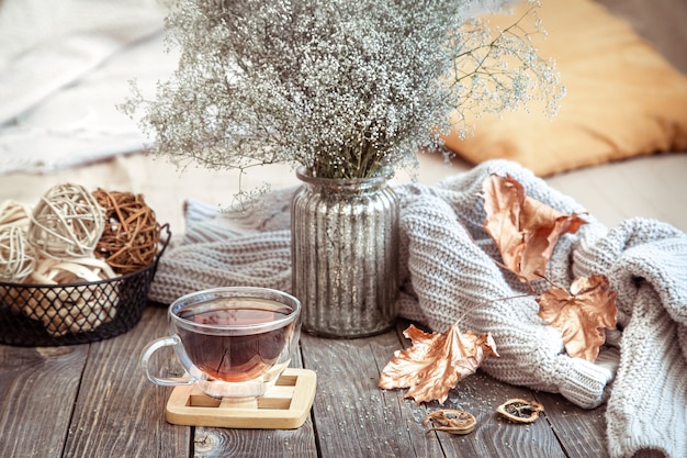 Taza de vidrio con té en la mesa de madera con detalles de decoración otoñal y flores secas en un jarrón.