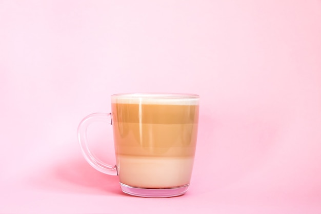 Taza de vidrio transparente de café con leche caliente sobre un fondo rosa suave.