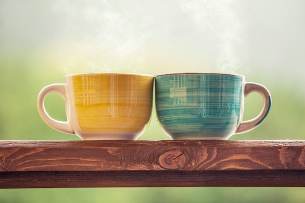 Tazas con una bebida caliente con té en un soporte de madera al aire libre en el campo