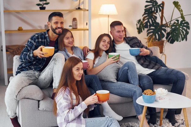 Con tazas de bebida Grupo de amigos hacen fiesta juntos en el interior