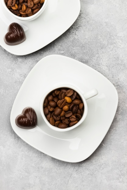 Tazas blancas para café expreso con granos de café y chocolate en forma de corazón sobre un fondo claro. Vista superior.