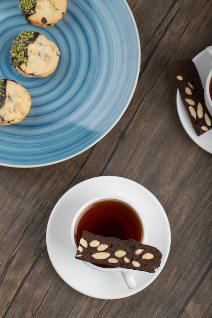 Tazas blancas de té caliente con tarta en rodajas colocada sobre la mesa de madera.