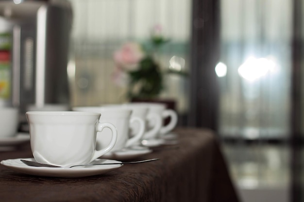 Las tazas blancas de té están en fila en la mesa con un mantel marrón