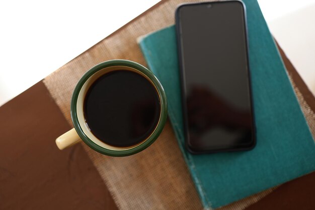 Tazas de café amarillas, teléfonos y libros sobre la mesa de madera dentro de la casa.