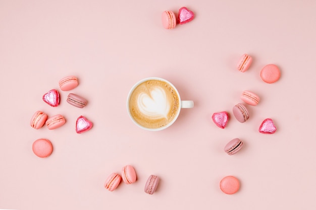 Tazas de café con caramelos y macarrones sobre fondo rosa pálido