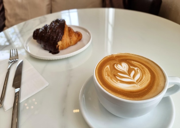 Tazas de café latte art caliente con un croissant