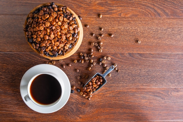 tazas de café negro y granos de café tostados en una mesa de madera