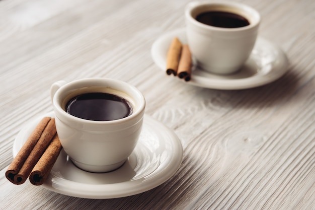 Tazas de café con palitos de canela sobre un fondo de madera blanco