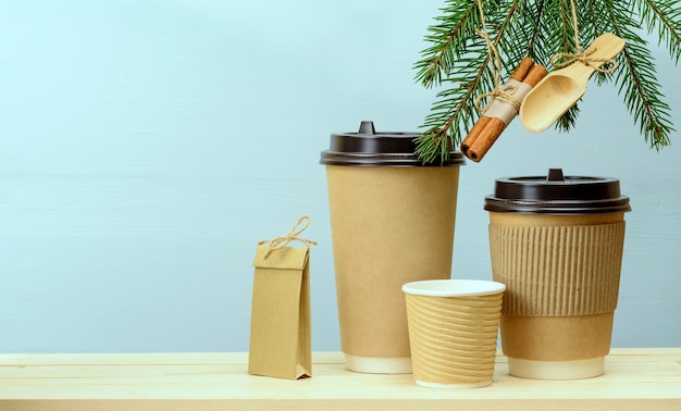 Tazas de café de papel artesanal y bolsa de papel en una mesa de madera con adornos navideños en abeto. Fondo de cafe navideño