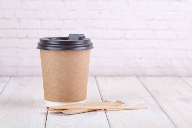 Tazas de café de papel artesanal en una mesa blanca cerca de fondo de pared de luz