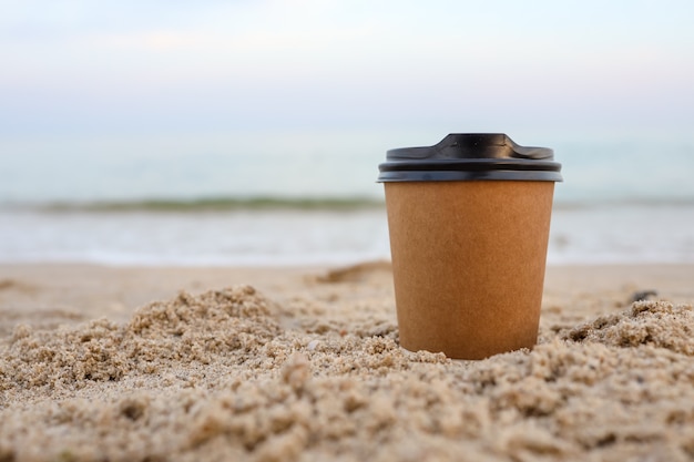 Tazas de café de papel tendido en la playa de arena en verano.