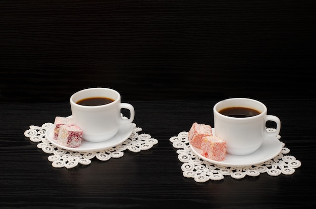 tazas de café en las servilletas de encaje y postre turco sobre un fondo negro