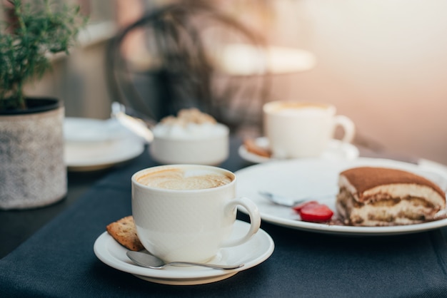 Tazas de café y tiramisú en mesa negro con hermoso arte latte en forma de corazón.